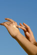 © Daryna  - Vertical image of female hands applying moisturizer to skin against blue sky background. Concept of texture and swatch of body care product, spa and aesthetics