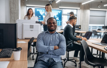 Wall Mural - Positive black man is smiling. Group of office workers are indoors together