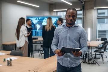 Wall Mural - Black man is with notepad. Group of office workers are indoors together