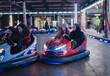 © qunica.com - A group of friends laughing and enjoying a lively ride on illuminated bumper cars during the evening inside a vibrant amusement park setting, creating a cheerful and festive atmosphere.