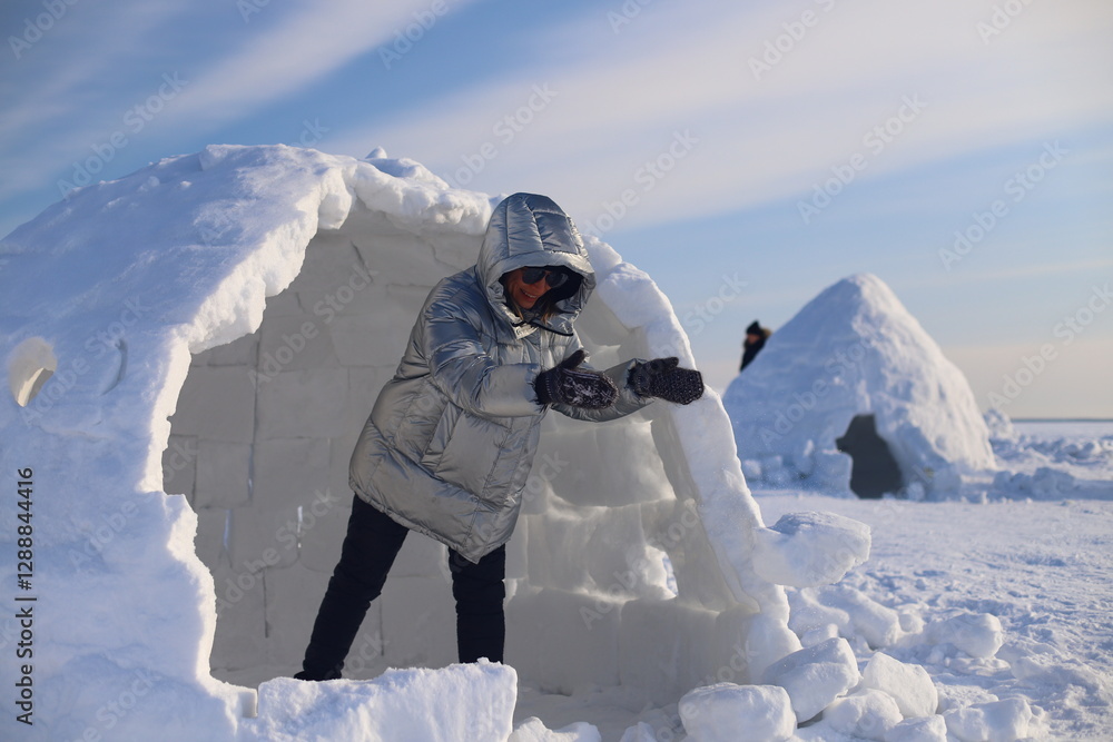 A happy adult woman builds an Igloo out of snow blocks in the Eskimo ...