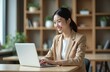 © Vadym - Happy young Asian businesswoman working with laptop in office. Cheerful attractive female entrepreneur using computer at desk. Confident pro types on keyboard. Corporate worker smiles, connecting,