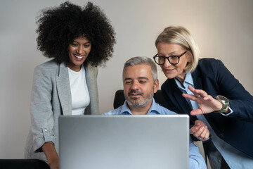 Wall Mural - Three busy happy middle aged professional business man and two women executive leaders team using laptop working on computer at work desk having conversation on financial project at meeting in office.