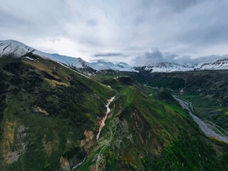 Wall Mural - green mountains in snow against snowy peaks, gorge in the mountains, aerial view