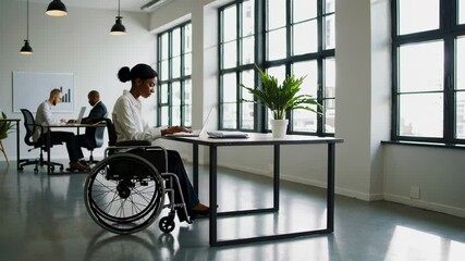 Aufkleber - Confident young disabled businesswoman using laptop while sitting in wheelchair in modern office with colleagues working in background in slow motion
