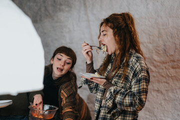 Poster - Two women share a casual meal together indoors, enjoying conversation and companionship, creating a warm and lively social atmosphere.