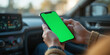 © Pixelbus - Hands holding a smartphone with a green mock-up screen inside a car, with a sharp foreground and blurred background, symbolizing technology and mobility.