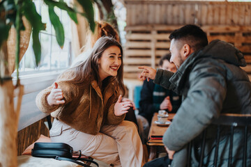 Wall Mural - A close-up shot of two friends enjoying a candid and cheerful conversation inside a warm and inviting cafe, surrounded by wooden decor and greenery.