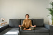 © Stock 4 You - Relaxed young indian woman sitting on couch, meditating with closed eyes in lotus pose. Peaceful latin hispanic or middle eastern brunette girl doing yoga, reduce stress on sofa at home. Copy space