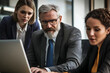 © Trendy Graphics - Multiethnic team of positive different aged colleagues watching Internet content on laptop together. Project manager showing online work project presentation on computer to happy coworkers