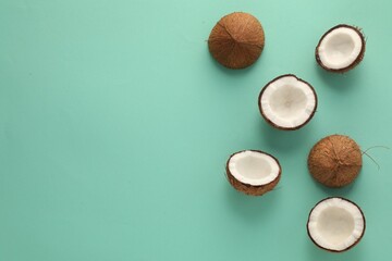 Wall Mural - Halves of fresh coconuts on turquoise background, flat lay. Space for text