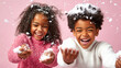 © MikeLegend - Two joyful children laughing and playing with snow against a pink backdrop during winter
