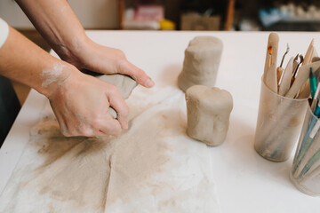 Poster - Hands of a female potter making ceramic clay product on the table in the pottery workshop. Potter is sculpting wet clay for ceramics products.