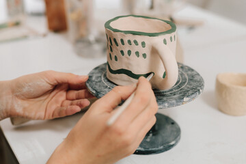 Poster - Painter is drawing and making a colorful decoration of a clay ware. Female artist is painting earthenware with paintbrush and water colors in the workshop.
