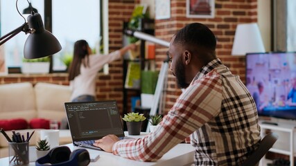 African american software developer works on programming code on a laptop in remote workspace. Productive IT engineer working on coding, software design and internet security innovation. Camera B.