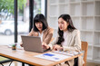 © Apichat - Two women are sitting at a desk looking at a laptop