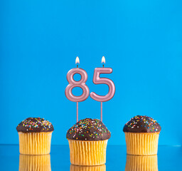 Wall Mural - Birthday candle with the number 85 - Three cupcakes on a blue background.