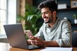© SimpleDesignStudio - Young South Asian Male Smiling While Using Smartphone and Laptop in a Bright Home Office Environment with Indoor Plants