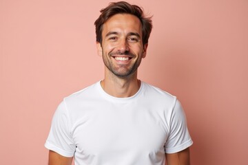 Smiling Young Caucasian Man in White T-Shirt Standing Against a Pink Background, Displaying Confidence and Approachability in a Casual Portrait Setting