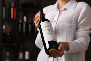 Wall Mural - Professional sommelier holding bottle of red wine indoors, closeup. Space for text