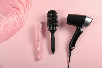 Wall Mural - Stylish round brushes, hairdryer and lock of dyed hair on pink background, flat lay