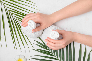 Wall Mural - Female hands with herbal massage bags and palm leaves on light background, closeup