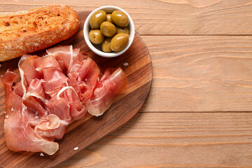 Canvas Print - Board with slices of tasty prosciutto, olives and bread on wooden background