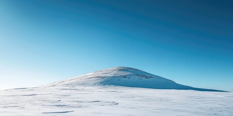 Wall Mural - Snow-covered hill on a clear blue sky day with minimal clouds, featuring a smooth hilltop and vast white landscape in foreground.