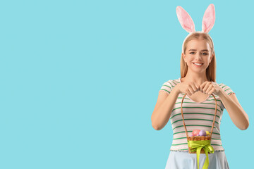 Wall Mural - Young girl with bunny ears and Easter basket on blue background