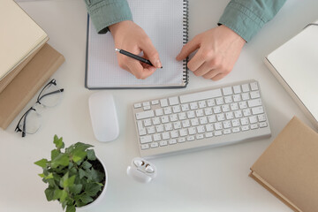 Wall Mural - Male student writing in clipboard while studying online on table, top view