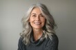 © imagemir - A smiling middle-aged woman with gray hair, wearing a cozy sweater, radiates warmth and confidence against a neutral background.