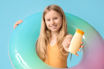 Wall Mural - Beautiful girl with bottle of sunscreen cream and inflatable ring on blue background