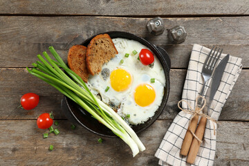 Wall Mural - Frying pan with tasty eggs, green onion and spices on wooden background