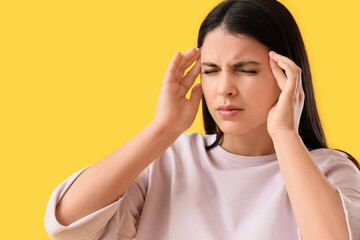 Young woman suffering from headache on yellow background, closeup