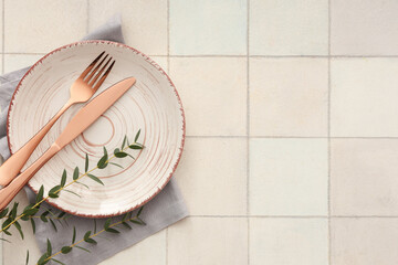 Wall Mural - Stylish table setting with plate, cutlery, napkin and plant branches on light tile background