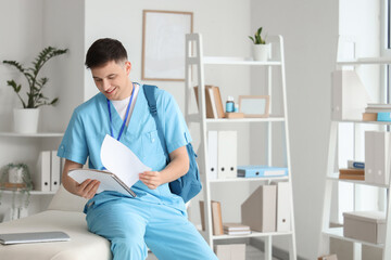 Wall Mural - Male medical intern with notebook sitting on couch in clinic