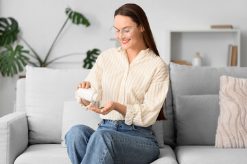 Sticker - Young woman taking spirulina capsules on sofa at home