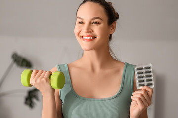 Wall Mural - Sporty young woman with spirulina capsules and dumbbell at home