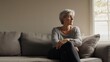 © Jorda - Stomach pain felt by a middle-aged woman sitting on a couch, clutching her stomach. Featuring discomfort and healing