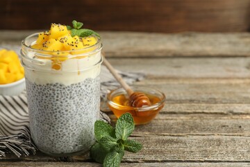 Wall Mural - Delicious chia pudding with mango in glass, mint and honey on wooden table, closeup. Space for text