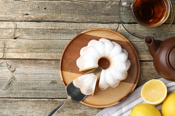 Wall Mural - Delicious lemon cake with powdered sugar, tea and citrus fruits on wooden table, flat lay. Space for text