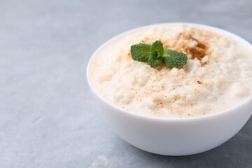 Wall Mural - Tasty rice pudding with cinnamon and mint in bowl on grey table, closeup. Space for text