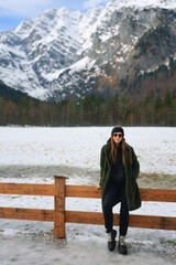 a woman standing near a wooden fence with snow-covered mountains in the background a woman in winter