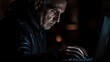 © Vitalii - A man is typing on a laptop in front of a window. The laptop is open and the man's hands are on the keyboard. There are several notebooks and a tablet on the desk