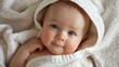 © Galib - A close-up of a baby wrapped in a white towel, looking at the camera.