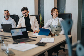 Wall Mural - A multicultural group of business people engaged in a meeting around a conference table. They are discussing ideas while using laptops and tablets in a modern office environment.