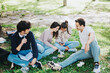 © qunica.com - Young students sitting on grass, engaging in a lively conversation and enjoying leisure time together. The setting is lush and green, reflecting a relaxed and friendly atmosphere.