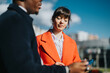 © qunica.com - A young man and woman are engaged in a business discussion outdoors under bright sunlight. The urban background indicates a modern and dynamic city environment with professional aspirations.