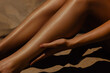 © Mirrorstudio - Sunlit close-up of female legs on sand with hand touching skin highlighting summer vibes. Skin care, sun protection