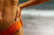 © Mirrorstudio - Female in orange swimwear standing by ocean. Skin care, sun protection